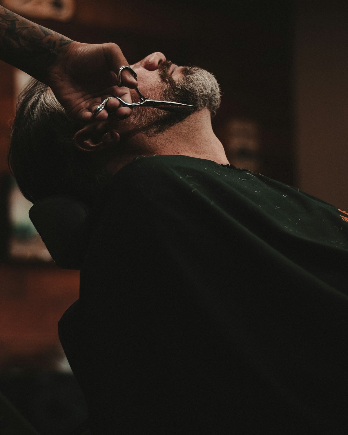 A barber working on a reclined customer, the shop dark behind them