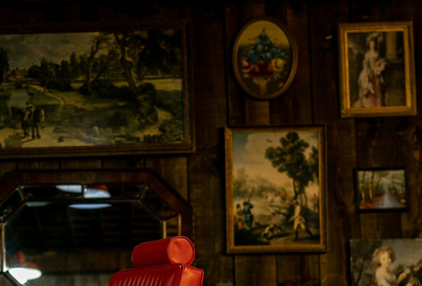The red chair in the back room, the wall behind it hung with framed pictures